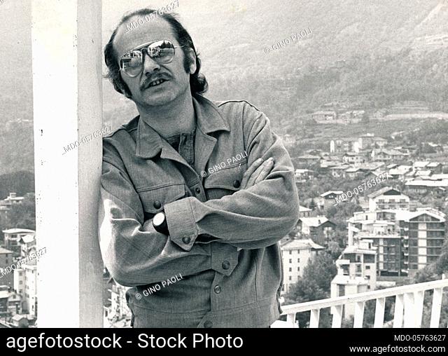 Italian singer-songwriter Gino Paoli leaning against a post with arms folded. 1970s