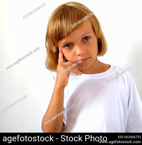 Little cute girl 6-7 years old with blond hair on a white background. Tanned skin. White T-shirt. Copy space. The girl raised her right hand and put her index...