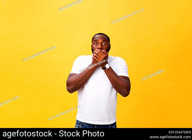 Amazed young African American hipster wearing white t-shirt holding hands in surprised gesture, keeping mouth wide open, looking shocked