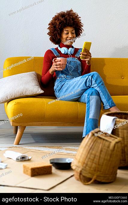 Young woman with coffee cup using mobile phone while sitting on sofa