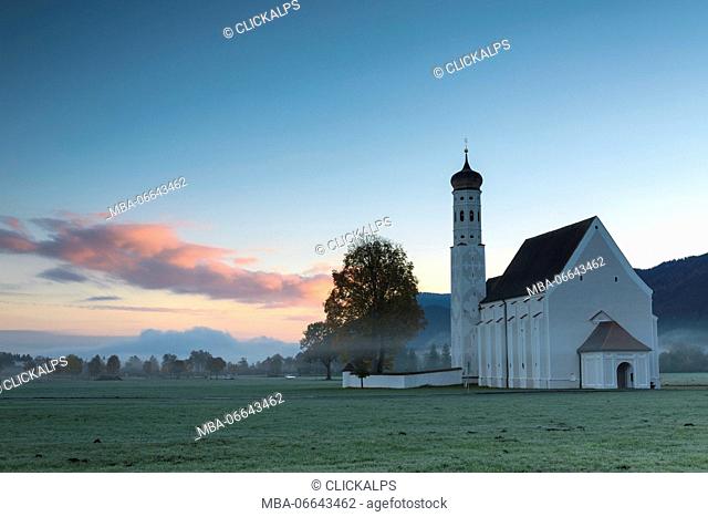 Pink clouds at sunrise on St Coloman Church surrounded by woods Schwangau Bavaria Germany Europe