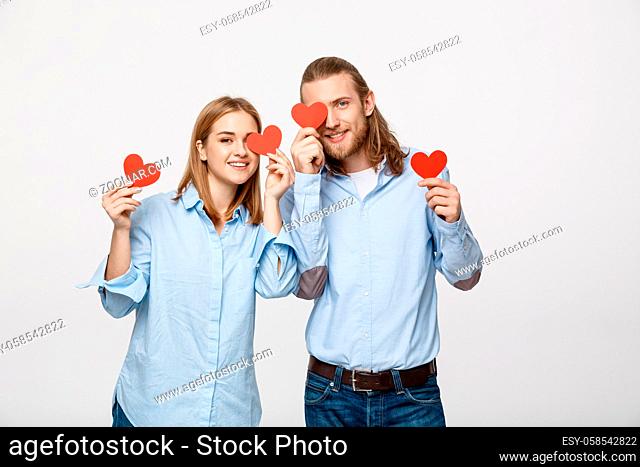 Attractive young in love couple holding red hearts over eyes on white background