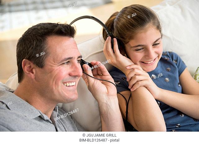 Smiling Caucasian father and daughter sharing headphones