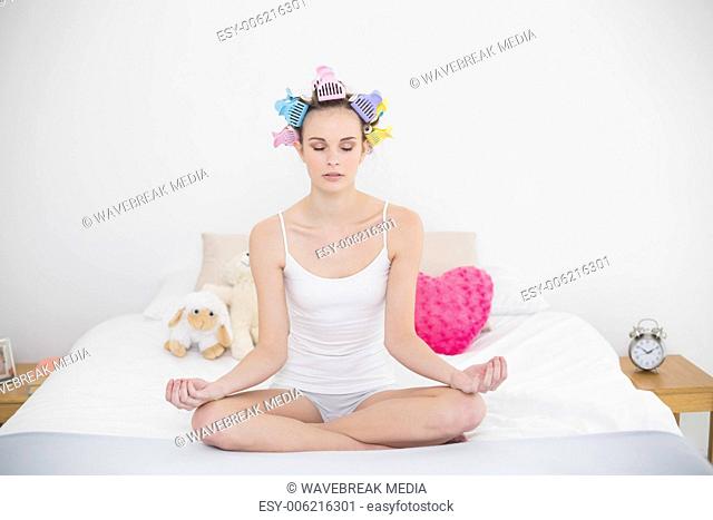 Calm natural brown haired woman in hair curlers practicing yoga