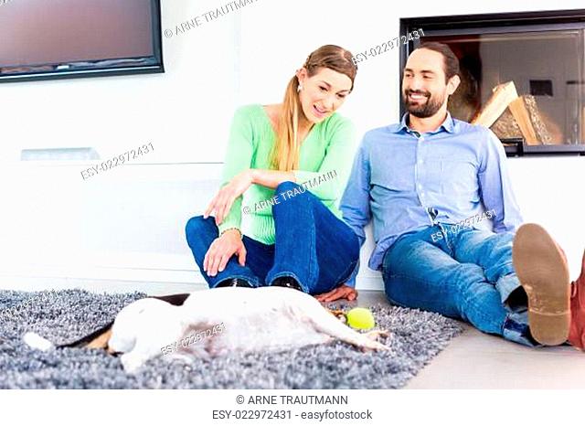 Paar sitzt im Wohnzimmer und spielt mit Hund