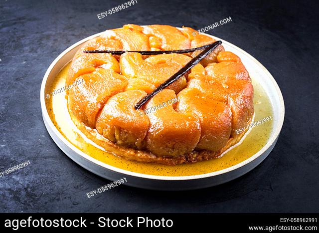 Traditional French tarte tatin with apples and vanilla offered as close-up on a modern design plate with rustic background