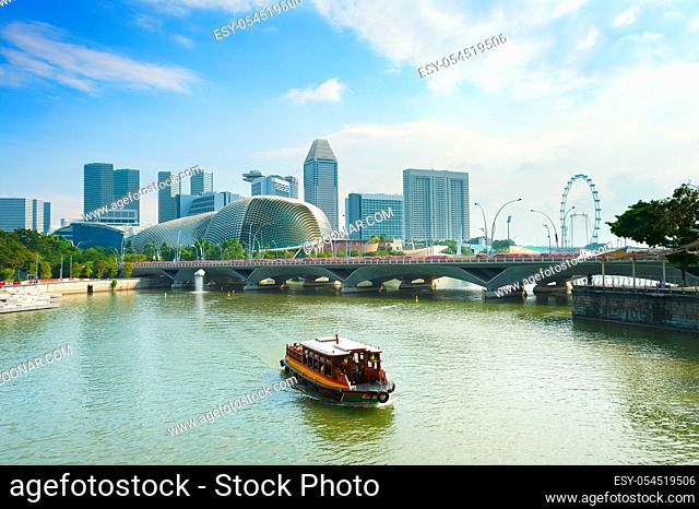 Touristic boat cruise by Singapore Marina bay harbor with ferris wheel flyer, Esplanade Theatres on the Bay and city skyline in background