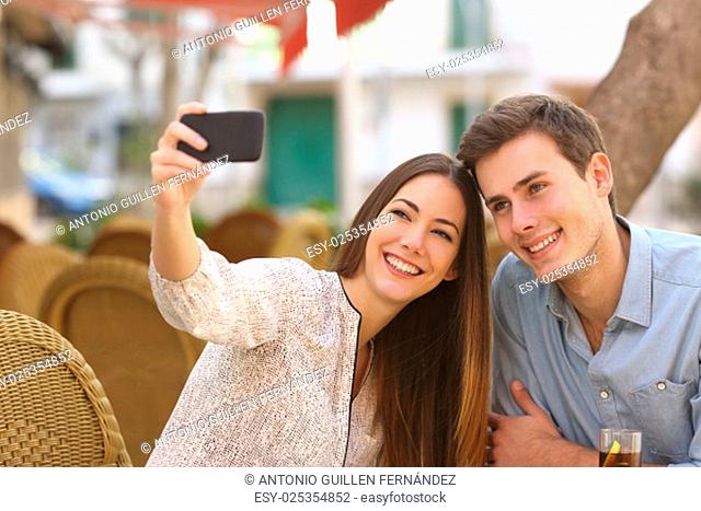 Happy couple taking a selfie photo with a smart phone in a restaurant terrace