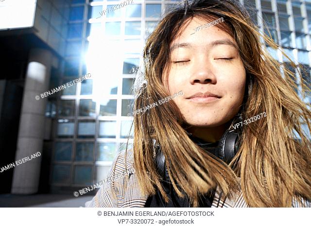 young emotional Asian woman with closed eyes in business district, in Paris, France