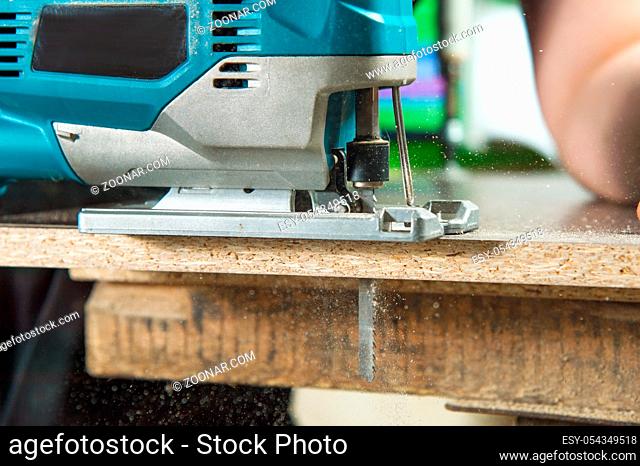 Close-up electric jigsaw for wood sawing a piece of wood and chips flying
