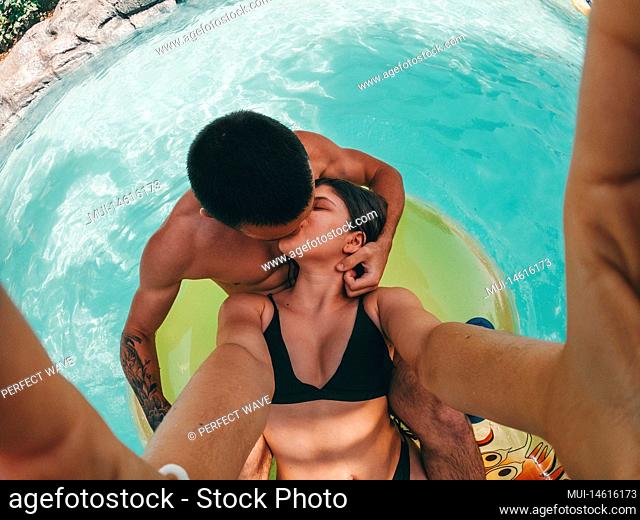 Couple of two happy people having fun and enjoying summer in an aquatic park with pool. Teenagers in love kissing each other