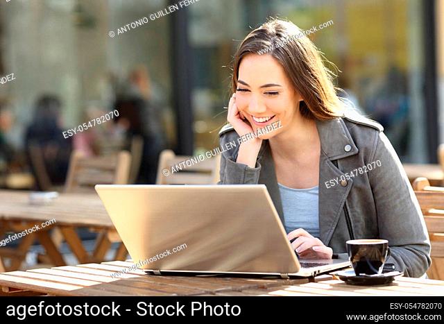 Happy woman watching media content online on laptop in a coffee shop terrace