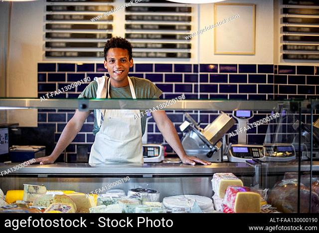 Smiling Latin American young man standing behind counter in cheese store