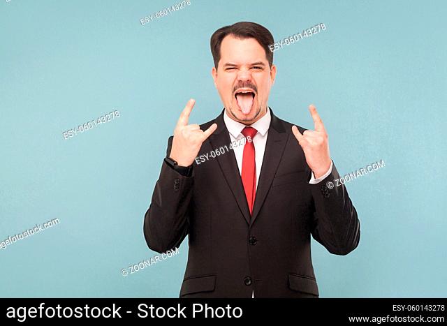 Emotional businessman showing rock sign. indoor studio shot. isolated on light blue background. handsome businessman with black suit