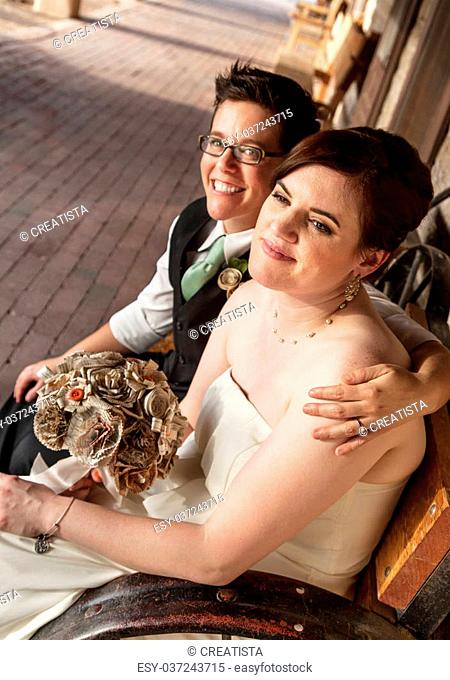 Smiling gay female couple sitting on rustic bench