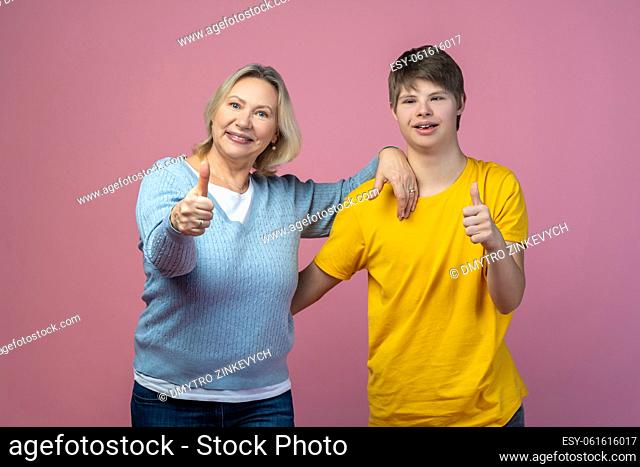 All excellent. Happy middle aged woman and guy with down syndrome showing ok sign smiling at camera on light background