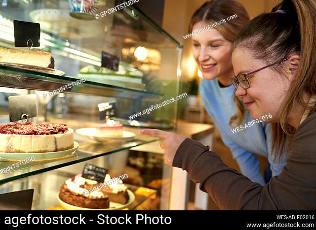 Happy coffee shop owner with down syndrome advising customer to choose cake in cafe