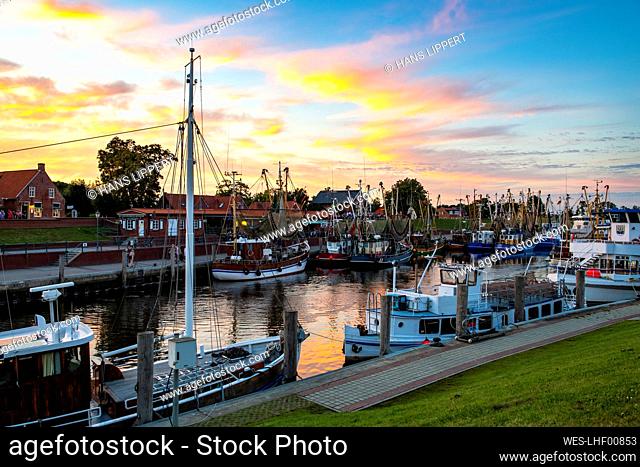 Germany, Lower Saxony, Greetsiel, Fishing boats moored along town harbor at moody dusk