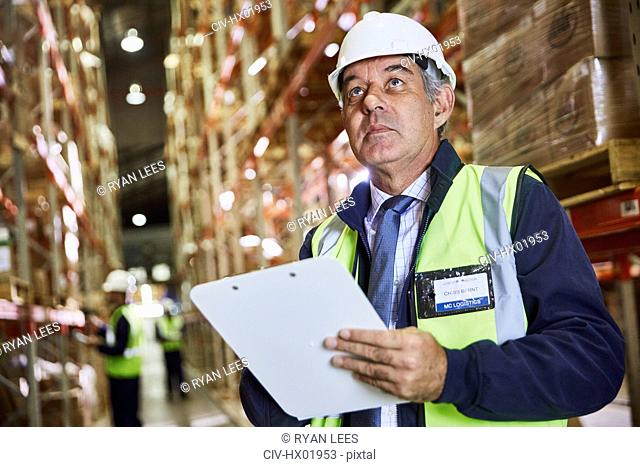 Manager with clipboard checking inventory looking up in distribution warehouse