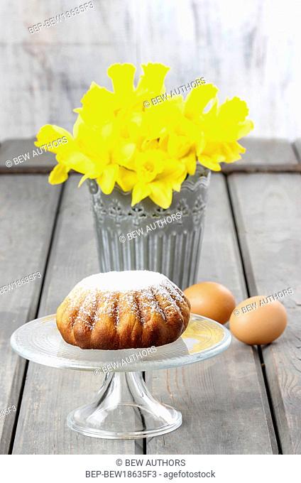 Daffodils in silver bucket on grey wooden table and easter yeast cake on cake stand