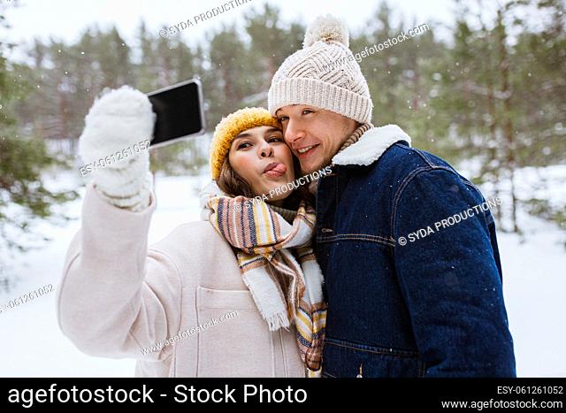 couple with smartphone taking selfie in winter
