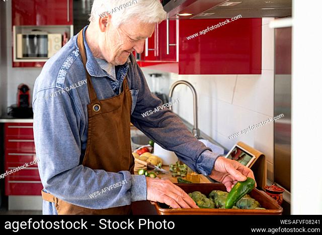 Senior man arranging vegetables while standing in kitchen at home