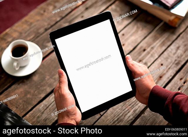 Man holds digital tablet computer in his hands. Closeup over cafe background - table, cup of coffee..