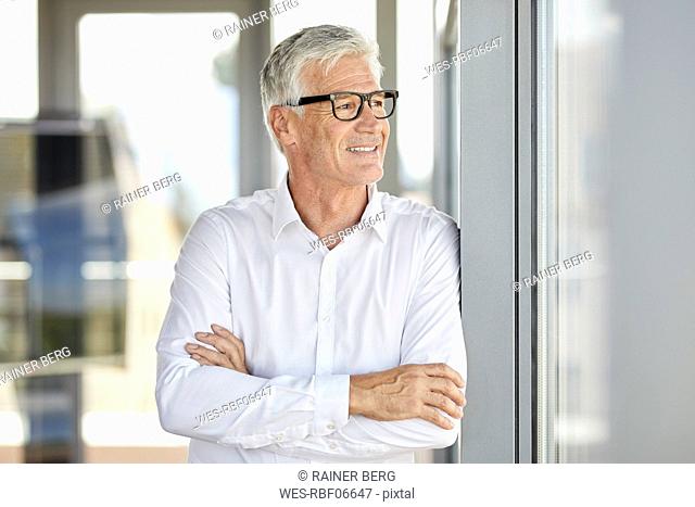 Businessman in office leaning against window, with arms crossed
