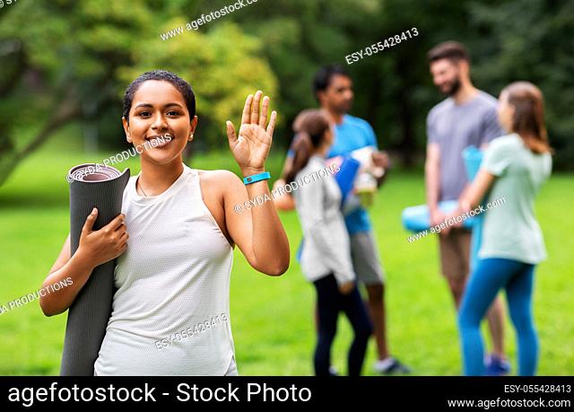 smiling woman with yoga mat waving hand at park