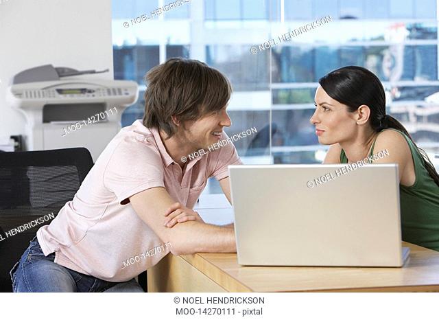Colleagues using laptop at desk in office