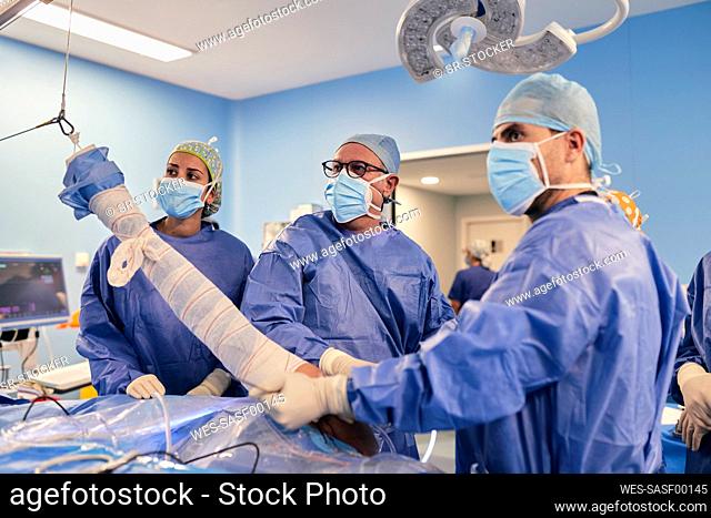Doctors wearing protective face mask operating surgery while standing in operation room