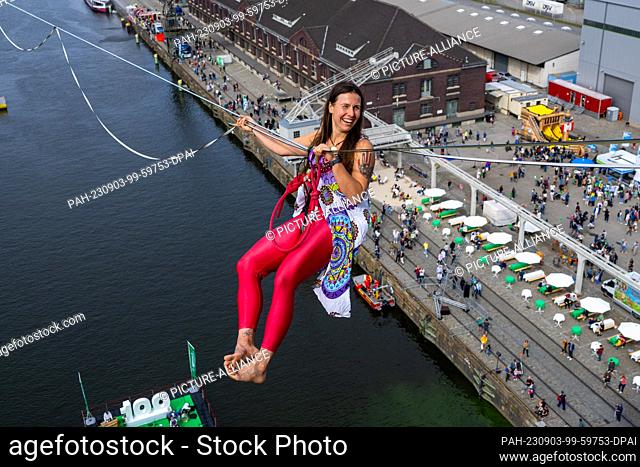 03 September 2023, Berlin: Rope acrobat Kasia hangs laughing on a high wire stretched between two towers at the celebration of the 100th anniversary of Berlin's...