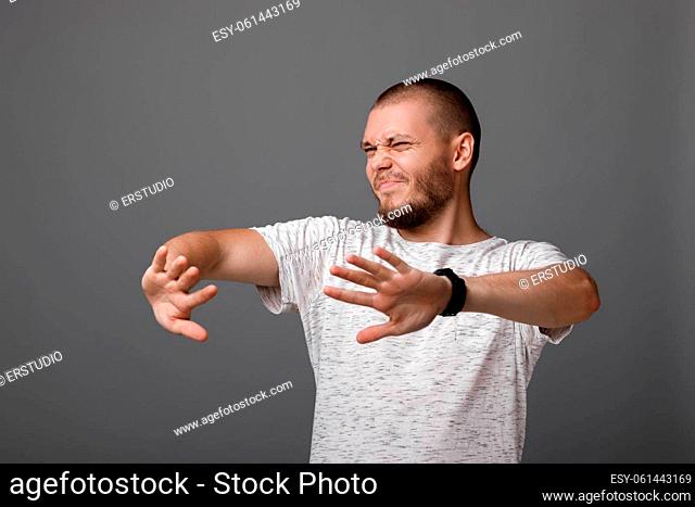 Portrait of frustrated young man showing stop gesture on gray background
