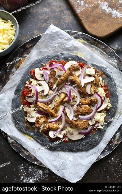Preparing black pizza with grilled chicken, mushrooms and red onions