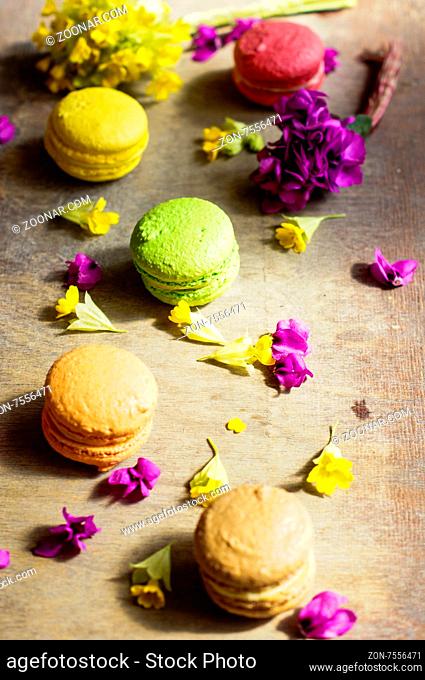Colorful macaroons and first spring flowers on old wooden background