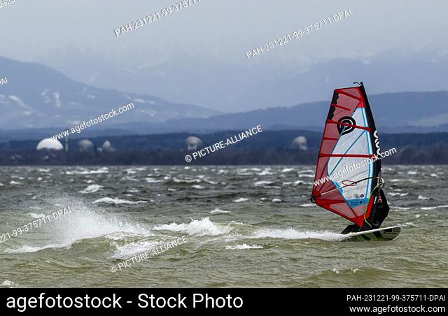 21 December 2023, Bavaria, Munich: A surfer takes advantage of the strong wind on Lake Ammersee near Herrsching for his leisure sport against the backdrop of...
