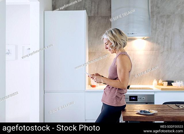 Mature woman using cell phone in kitchen at home