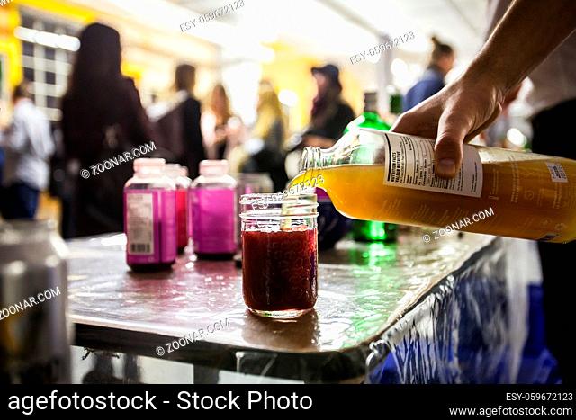 Man making a delicious drink by pouring kombucha into a glass of wildberry juice in an industrial environment
