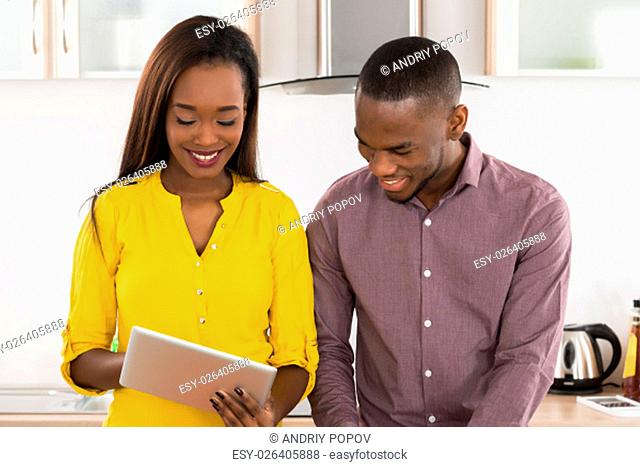 Young African American Couple Using Digital Tablet In Kitchen For Recipe