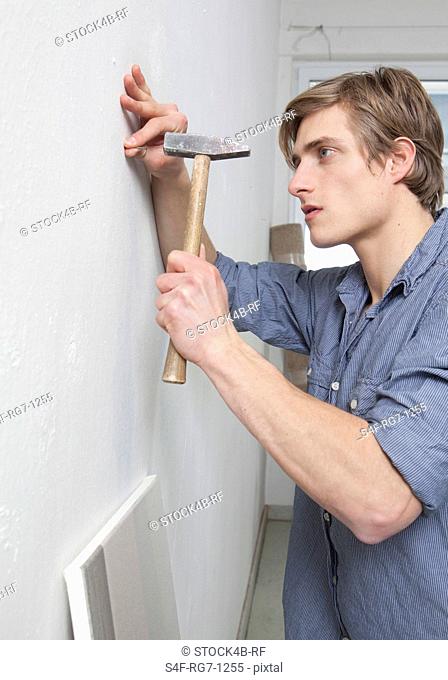 Young man with hammer and nail at wall