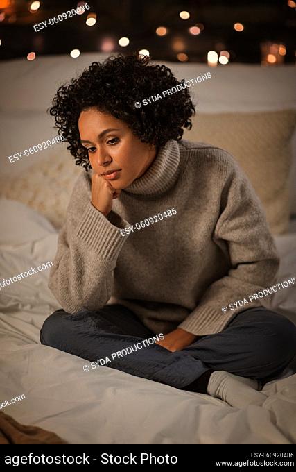sad woman in sweater on bed at home at night