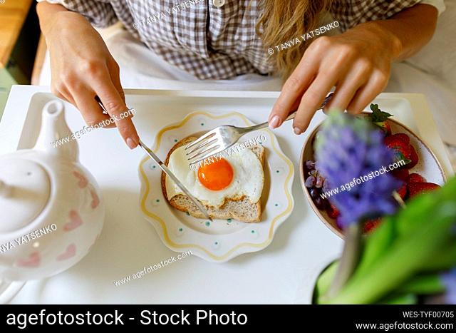 Woman cutting fried egg on toast at home