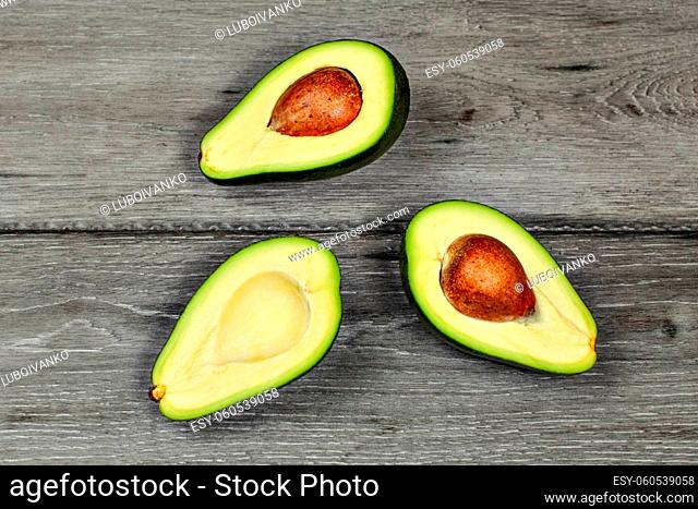 Tabletop view - three halves of cut avocado, some with seed pit, on gray wood desk
