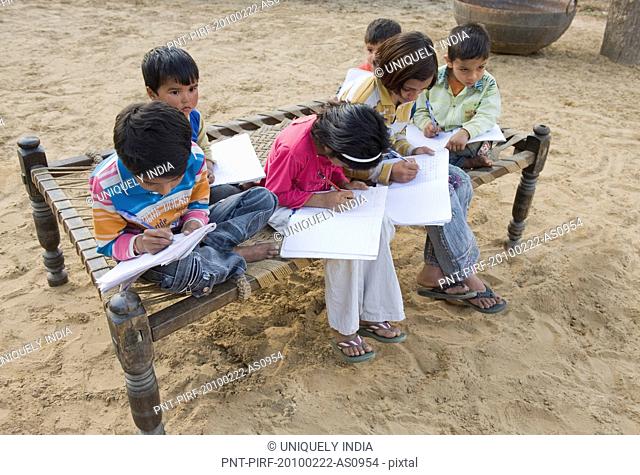 Children doing homework on a cot, Hasanpur, Haryana, India