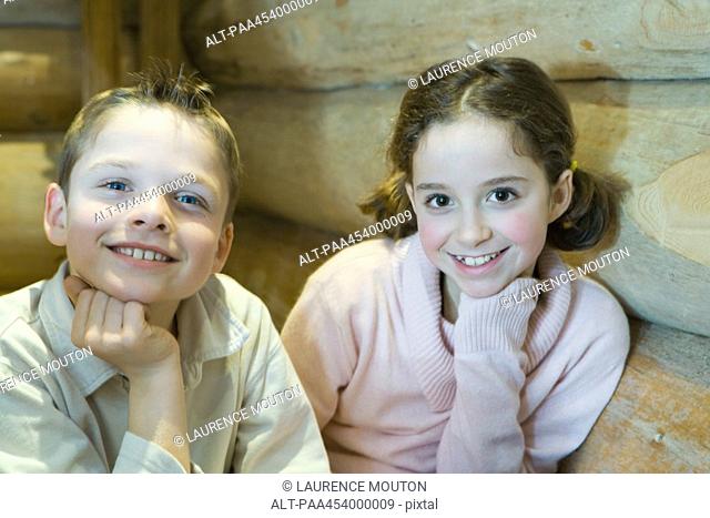 Boy and girl sitting side by side, hand under chin, smiling at camera