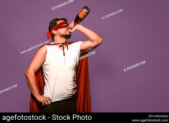 Super antihero man drinks alcohol from the throat of a bottle. Isolated on grape purple background with copy space or textspace at right side