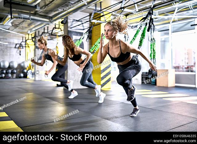 Slim girls are training intensive with goflo-trainers in the gym on the windows background. They are wearing the multicolored sportswear: pants