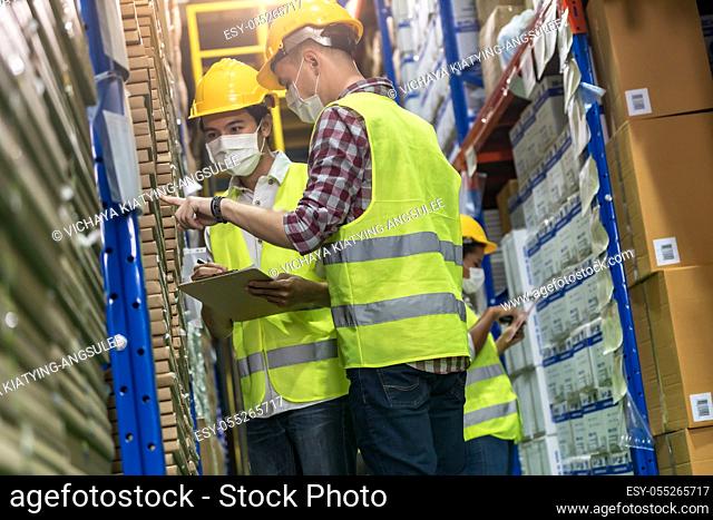 Interracial team Asian African and Caucasian work check goods use clipboard barcode scanner in distribution center. They wear face mask prevent from COVID-19