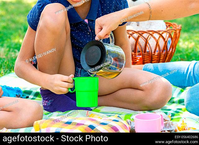 Close-up as a girl pours tea into a teenager's cups on a picnic in the park