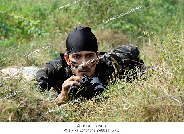 Soldier lying in a forest with binoculars